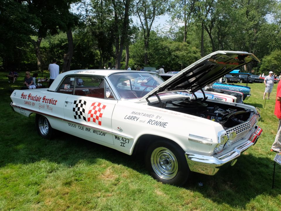 White 1963 Chevrolet Impala with racing decals and hood open, parked on grass