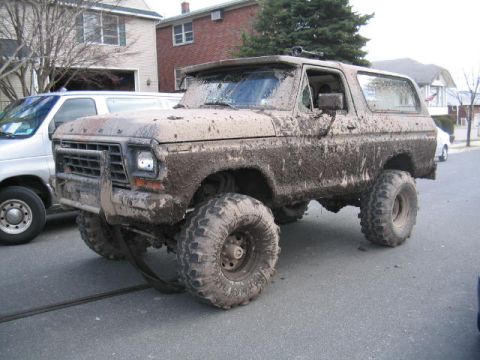 1979 Ford Bronco - Mud-covered 1978 Ford Bronco with large off-road tires parked on a street.