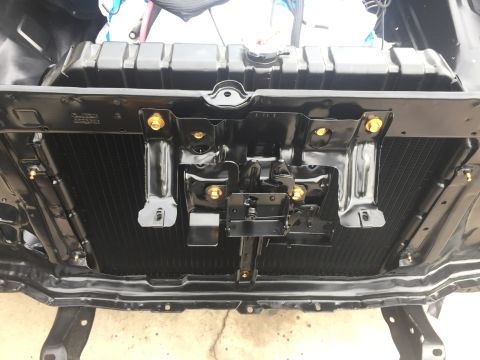 1978 Ford Bronco - Close-up of a vehicle's radiator and its mounting hardware, showing black metal components and gold fasteners.