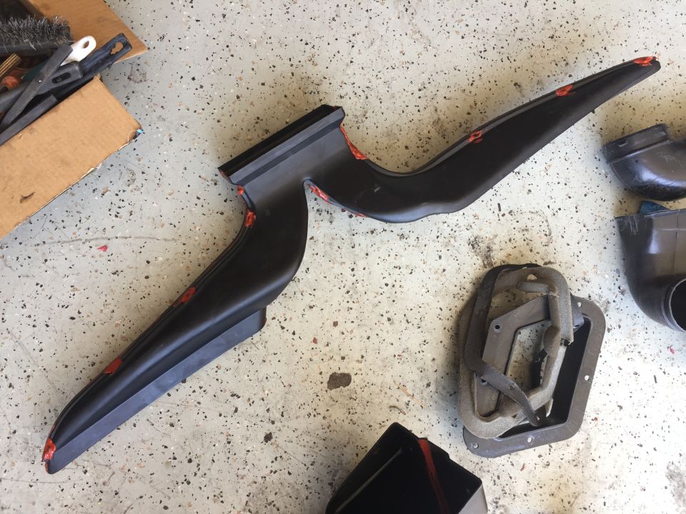 Black plastic HVAC ducting and a rubber seal on a garage floor. Box of brushes in background