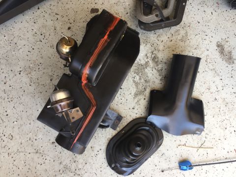 1978 Ford Bronco - Various black car parts, including heater core components and a shifter boot, are displayed on a concrete surface.