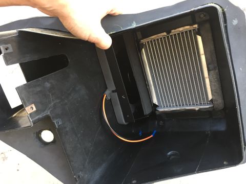1978 Ford Bronco - A hand holds the edge of a black plastic housing containing a metal heater core and wiring.