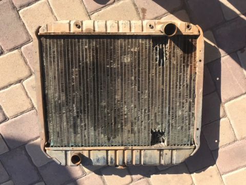 1978 Ford Bronco - A used radiator, showing significant damage to its fins and a large hole, lies on a paved surface.