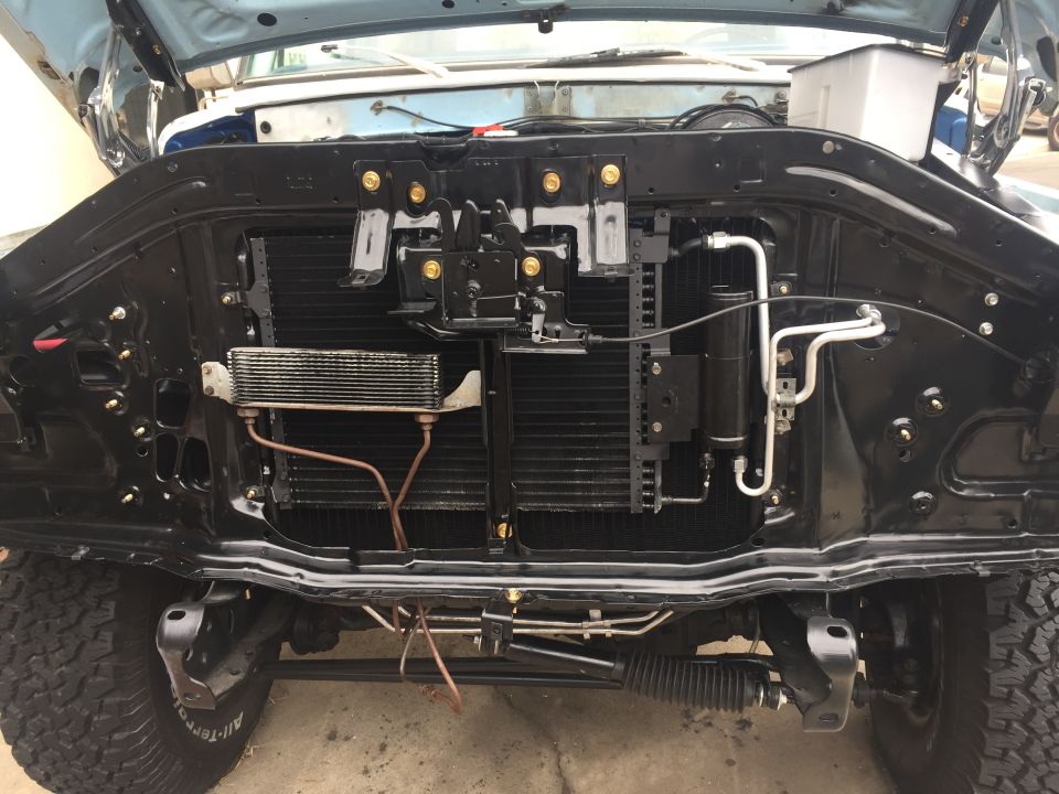 Front of vehicle showing radiator, AC condenser, and engine components. Tires visible