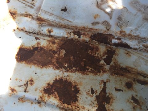 1978 Ford Bronco - Close-up view of a heavily rusted white metal panel, showing significant corrosion and wear.