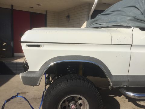 1978 Ford Bronco - Close-up side view of a white SUV's front fender and wheel assembly.