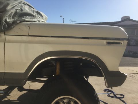 1978 Ford Bronco - Side view of a white SUV's fender and tire, partially obscured by a gray tarp.