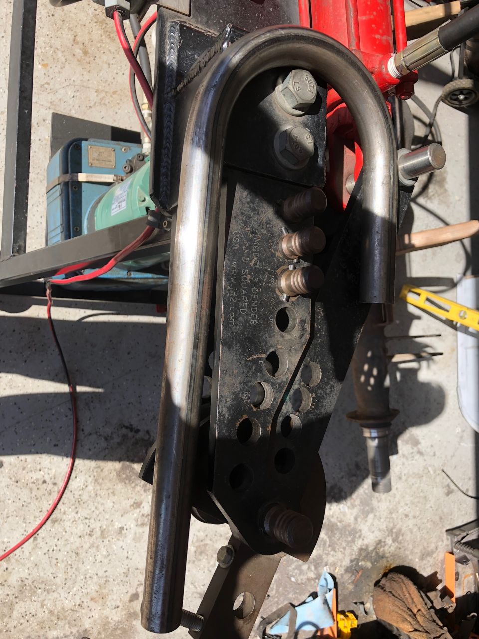 Close-up of a bent metal tube attached to a black bracket with bolts. Text on bracket reads 'WWW.H2.COM'