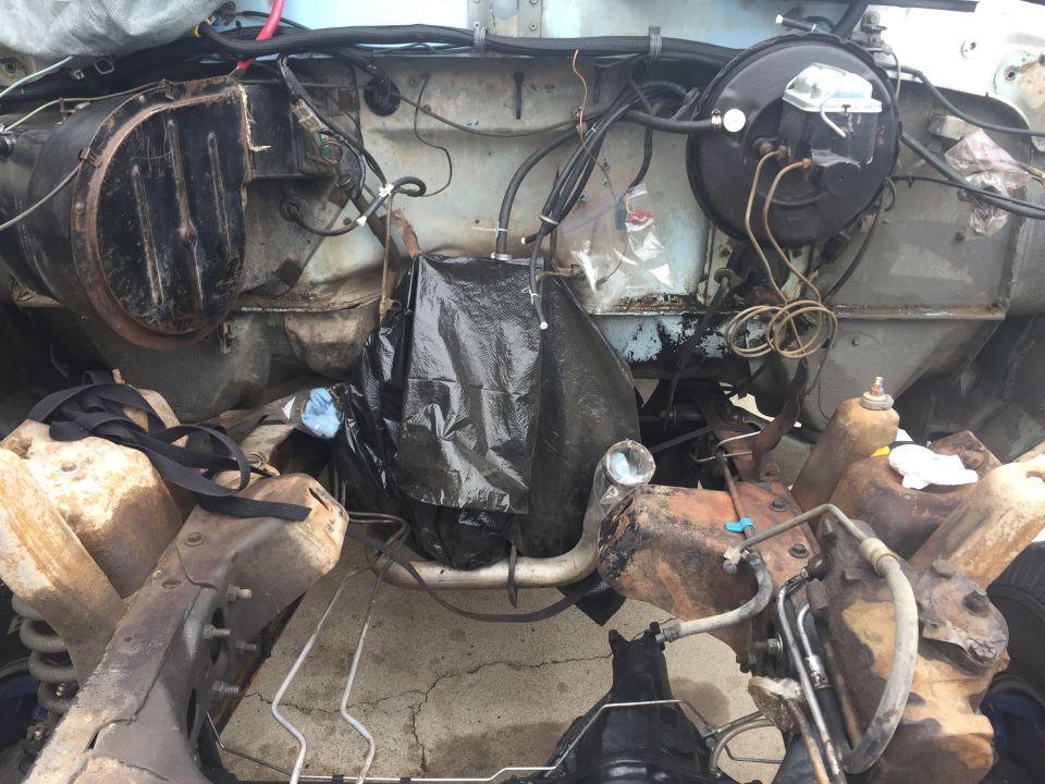Engine bay with parts covered in black plastic, brake booster, and exposed frame