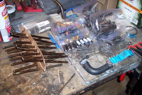 1995 Ford Bronco - Various engine components are laid out on a cluttered workbench, ready for assembly or repair.