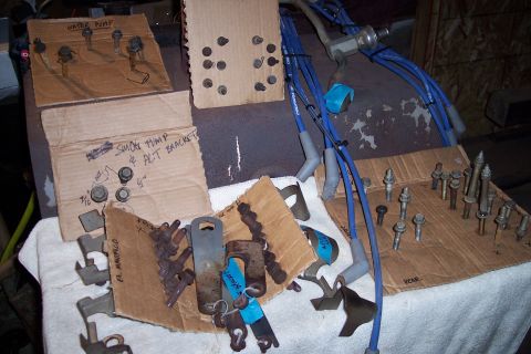 1995 Ford Bronco - Various automotive parts, including a water pump and smog pump bracket, are laid out with hardware on cardboard.