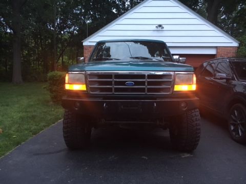 1996 Ford Bronco - Front view of a green Ford truck with its hazard lights on, parked in a driveway.