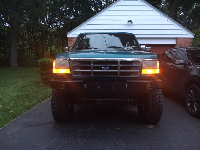 Green Ford truck with aftermarket bumper, parked in driveway next to another SUV