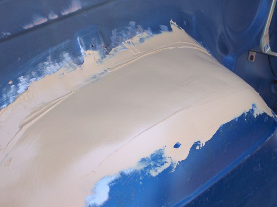 Body panel being filled with putty, showing blue paint underneath