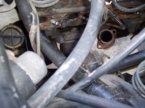 1990 Ford Bronco - Tight engine-bay shot down the side of a V8 with the exhaust manifold removed, exposing bare spark plugs in the cylinder head and a rusty e…