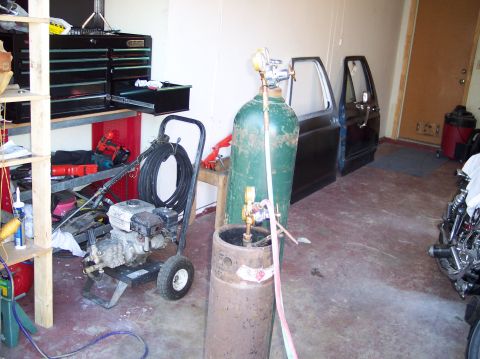 1990 Ford Bronco - A home garage workspace with a green oxygen cylinder and rusty acetylene tank with regulators and torch hoses in the foreground, a Honda-po…