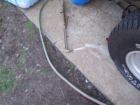 1990 Ford Bronco - Oxy-acetylene cutting torch in use, with sparks spraying near a vehicle tire.