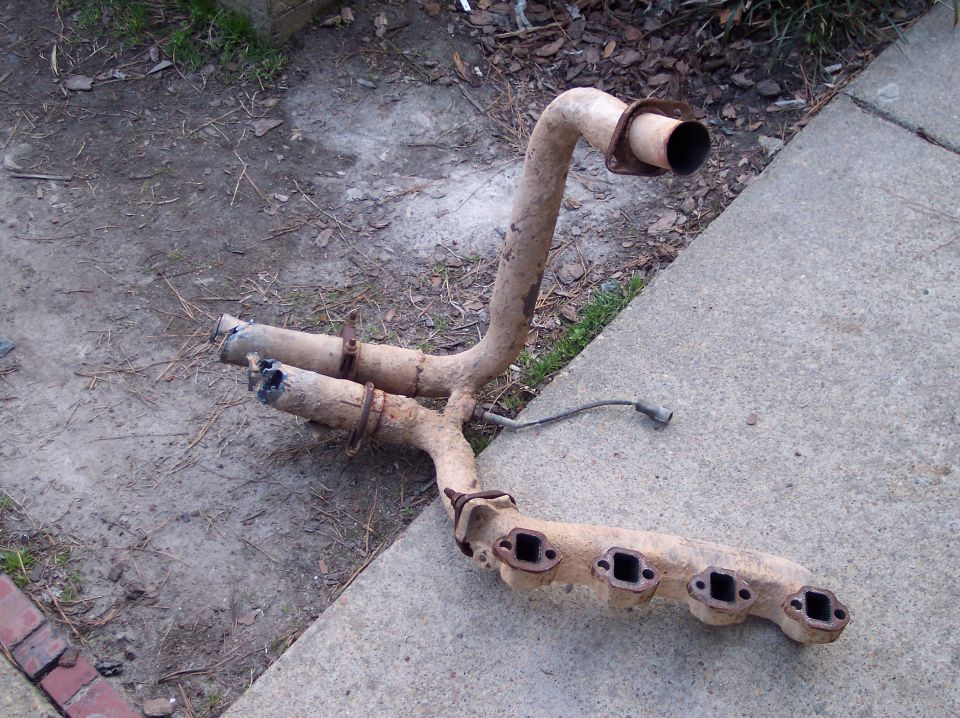 Rusty exhaust manifold with four exhaust ports and two pipes leading to a single outlet