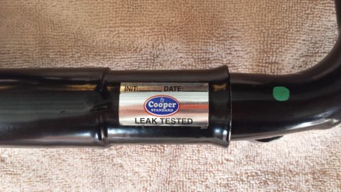 2005 Mercury Grand Marquis - A black metal pipe is shown with a Cooper Standard label indicating it has been leak tested.
