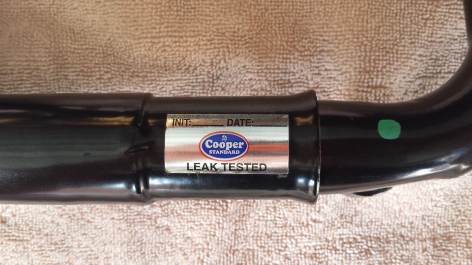 Black metal pipe with Cooper Standard leak tested label