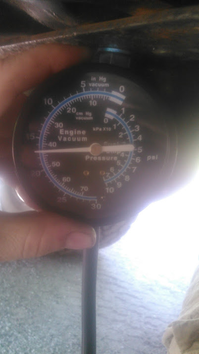 1992 Ford Bronco - A hand holds an engine vacuum and fuel pressure test gauge with a black face, marked in inches of mercury, cm Hg, kPa and psi, with the nee…