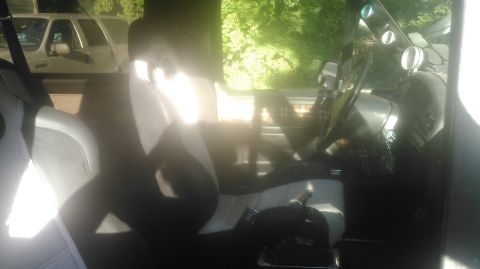 1992 Ford Bronco - Sun-flared interior shot taken through an open door showing a pair of gray and black cloth bucket seats fitted in a truck cab. A center-mou…