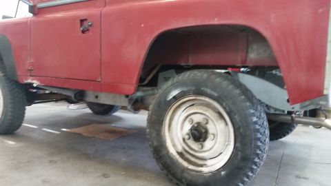 1984 Land Rover Defender - Side view of a red 1984 Land Rover Defender 90, revealing its chassis and wheel assembly.