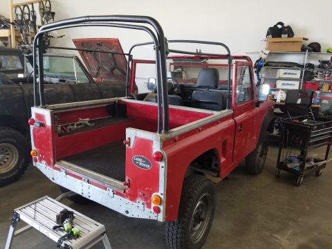 1984 Land Rover Defender - A red Land Rover Defender is shown in a garage with its rear end facing the camera, next to another vehicle.