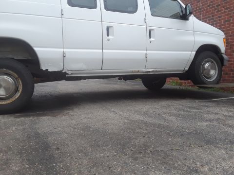 1999 Ford E250 - This white van shows significant rust and wear along its lower body panels.