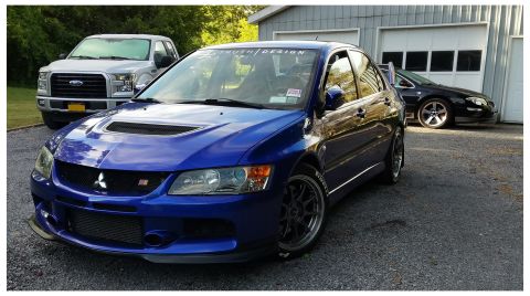 2006 Mitsubishi Evolution - A blue 2006 Mitsubishi Lancer Evolution IX is parked in front of a garage with a pickup truck and another car.
