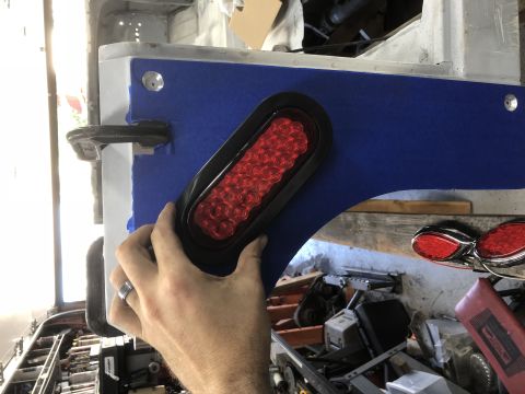 1992 Jeep Wrangler - A hand holds a red LED trailer light, preparing to install it on a vehicle's body, which is covered in blue tape.