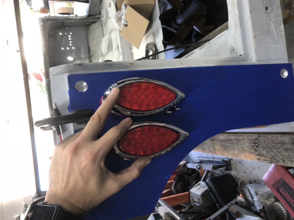 Hand holding custom red LED taillights against blue panel on vehicle body