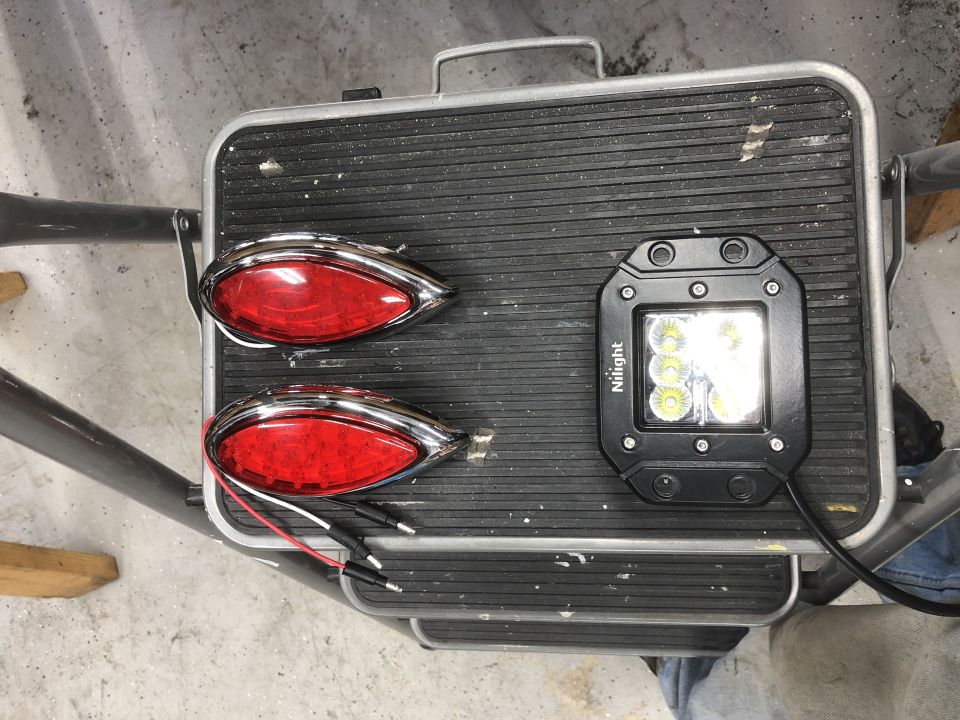 Two red oval tail lights with chrome trim and a square Nilight LED light bar on a black textured surface