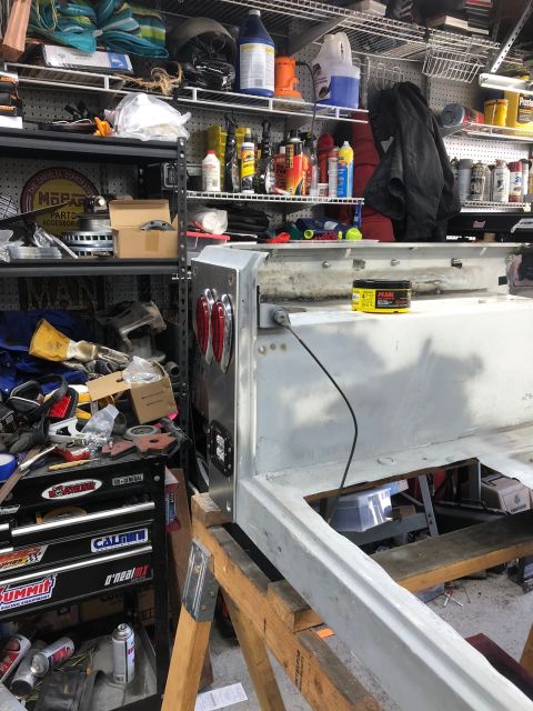 1992 Jeep Wrangler - The rear section of a vehicle frame, taillights and electrical wiring, is shown supported by sawhorses in a cluttered garage.