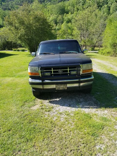 1996 Ford Bronco - Front view of a dark blue 1996 Ford Bronco parked on a gravel driveway with a grassy yard and trees in the background.
