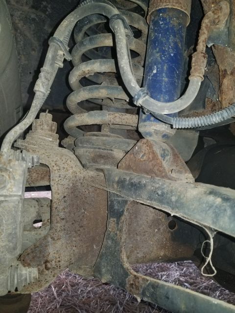 1996 Ford Bronco - Close-up view of heavily rusted vehicle suspension parts, including a coil spring and shock absorber.