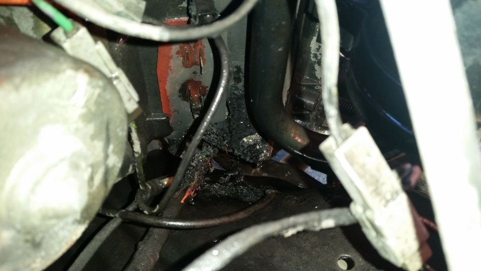 Close-up of melted wiring and damaged components in an engine bay