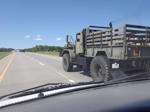 1994 Ford Bronco - A military truck drives down the highway on a sunny day, with another vehicle visible in the distance.