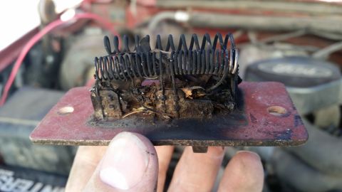 1985 Ford Bronco - A burnt blower motor resistor is shown, with visible damage to the coil and base. The vehicle's engine bay is blurred in the background.