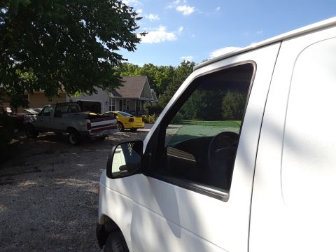 1999 Ford E250 - A white van is parked in a driveway with other vehicles visible in the background.
