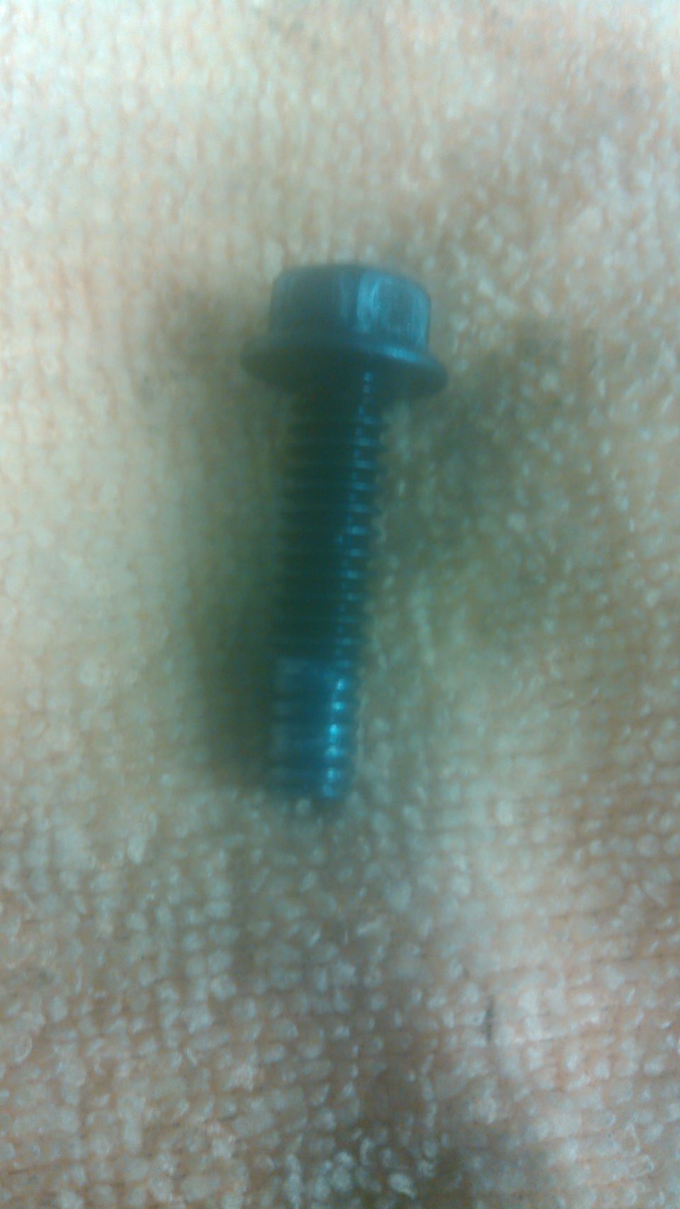 Close-up of a black flange hex bolt with damaged threads on a paper towel