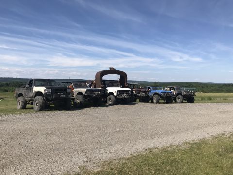 1989 Ford Bronco - Several modified off-road vehicles are parked together in a rural setting on a sunny day.