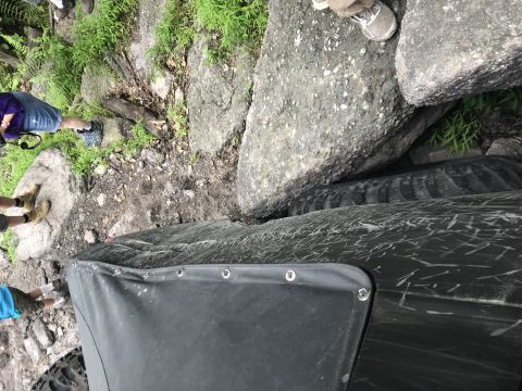 1989 Ford Bronco - An off-road vehicle navigates a challenging rocky terrain, with its tire tightly wedged between large boulders.