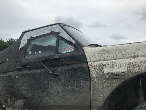 1989 Ford Bronco - A heavily muddied Ford F-250 shows damage to its window, covered with plastic and tape.