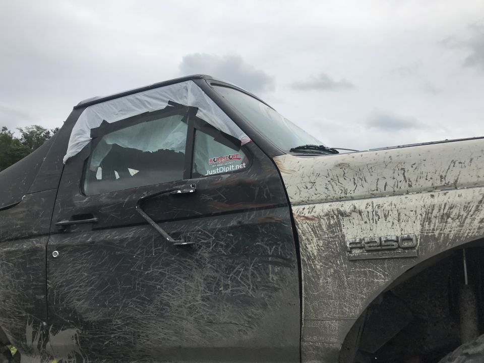 Mud-covered Ford F-250 side view with plastic-taped window and a "JustDipIt.net" sticker