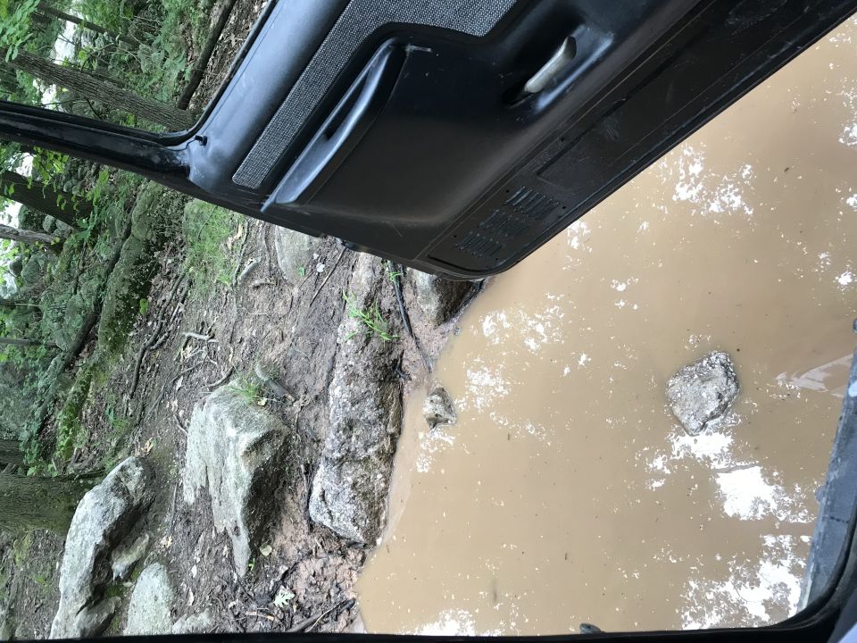 Black interior door panel above muddy water and rocks