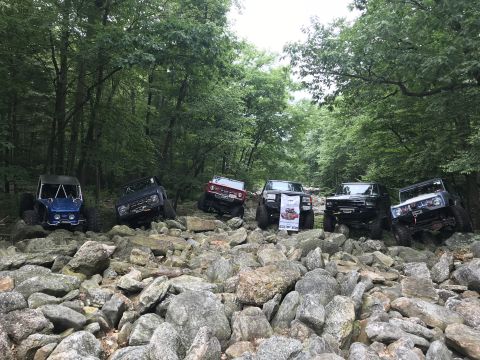 1989 Ford Bronco - Multiple off-road vehicles traverse a challenging rocky terrain in a forest setting.