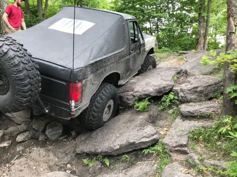 1989 Ford Bronco - This modified Bronco navigates a challenging rocky trail with a person watching nearby.
