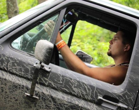 1989 Ford Bronco - A man drives a heavily mud-splattered SUV, with the side mirror and interior visible.