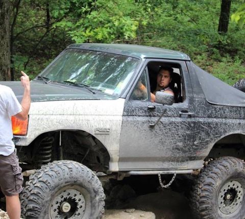 1989 Ford Bronco - A heavily modified Ford Bronco navigates an off-road trail with a driver and passenger visible.